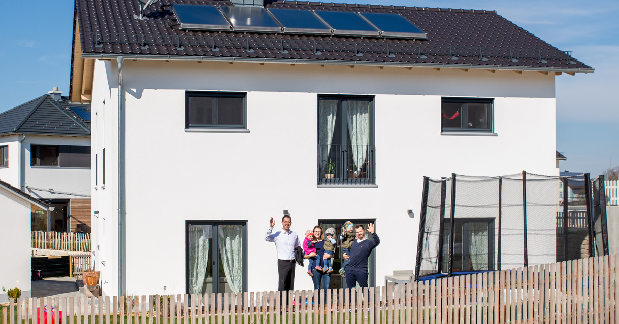 Eine Familie mit drei Kinder stehen vor einem weißen Haus.